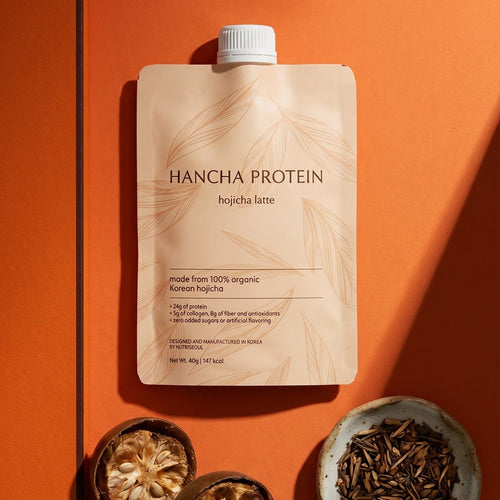 Hancha Protein world's best tasting and cleanest hojicha latte package on an orange background with dried hojicha leaves.